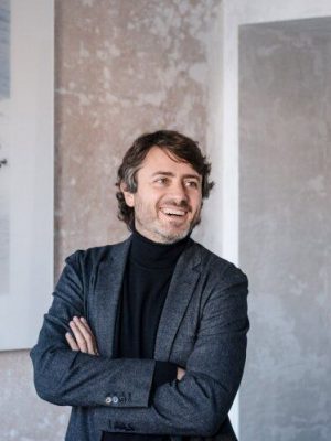 Gabriele Salini arms crossed smiling with concrete walls background
