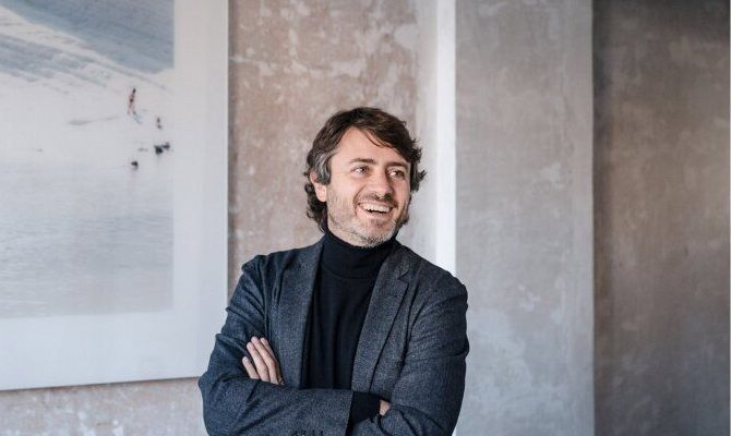 Gabriele Salini arms crossed smiling with concrete walls background