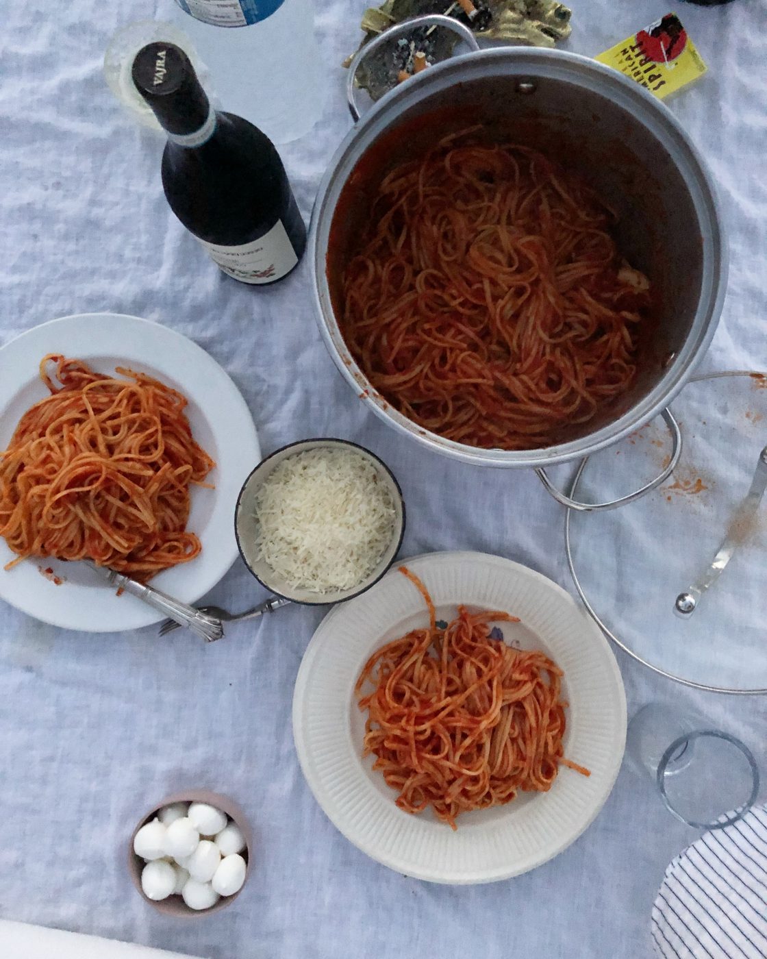 an overhead photo of spaghetti pomodoro in two bowls and in the pot along with a bowl of parmesan and a bottle of wine