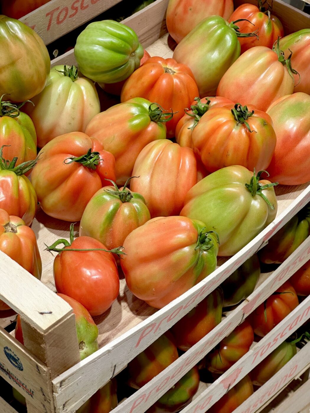 a stack of cases of cuore di blue tomatoes in various stages of ripening colors