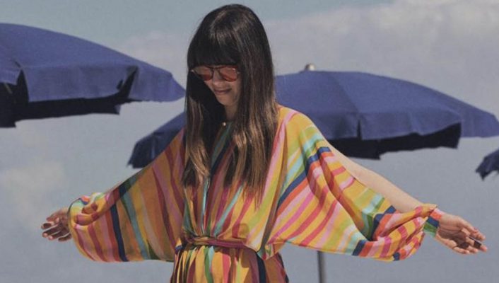 Caterina Licitra Ponti wearing a colorful dress and sunglasses posing in italian beach with blue umbrellas