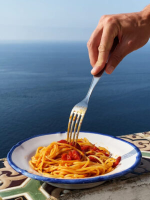 someone twirling a fork into spaghetti al pomodoro perched on the terrace overlooking the sea