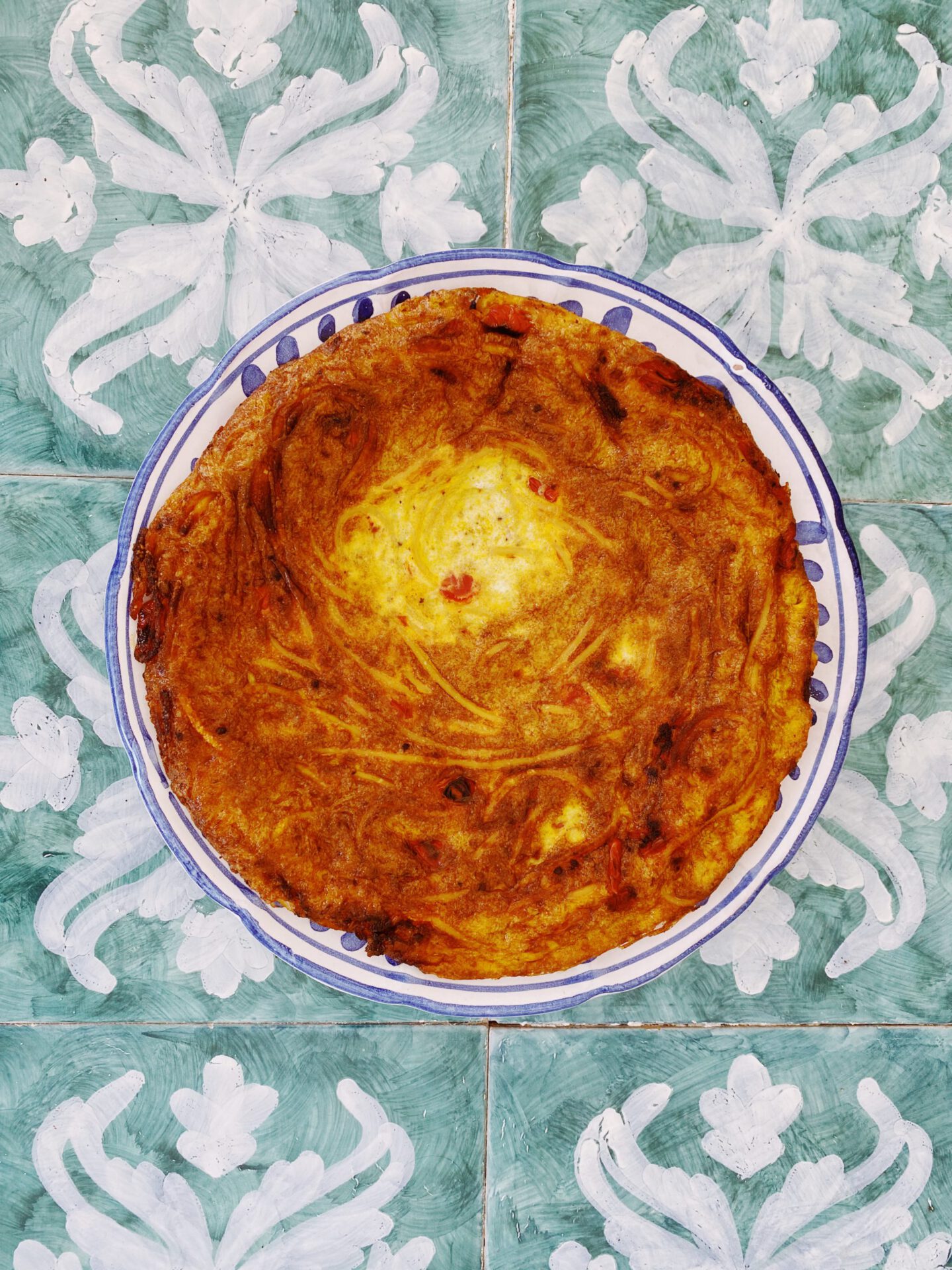 Frittata di pasta over blue ceramic plate and blue decorated background in Italy
