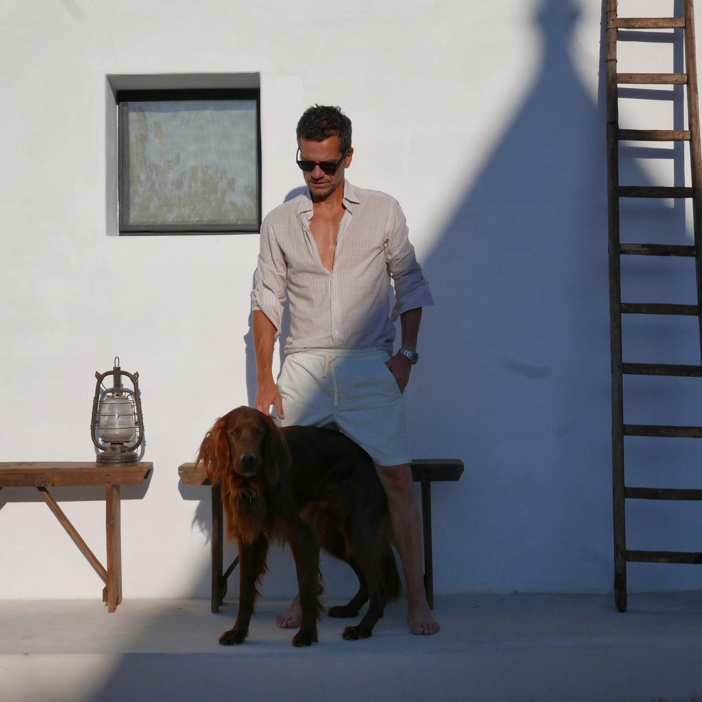 Costantino Affuso with summer clothes and dog posing in front of white wall with stairs and wooden table in Italy