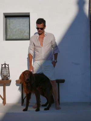 Costantino Affuso with summer clothes and dog posing in front of white wall with stairs and wooden table in Italy
