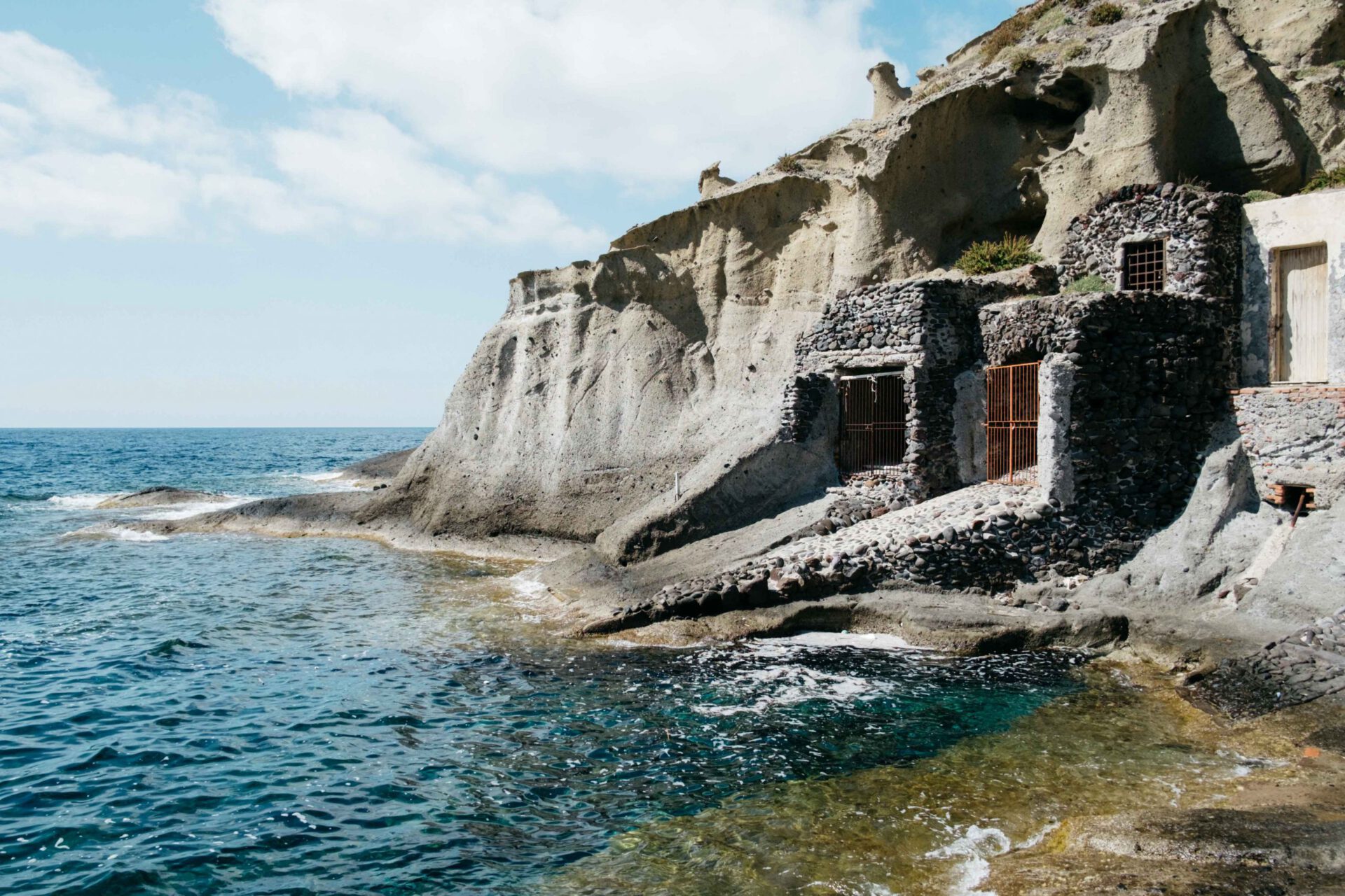 Rocky cliff over blue sea with windows and door in the rocks in Salina Sicily in Italy