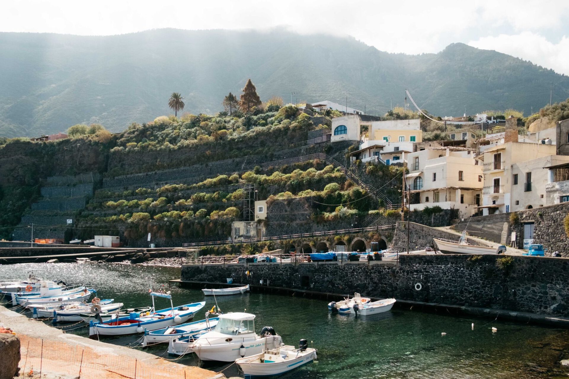 Small port with boats with cliff and rocky mountains behind and white houses in Salina Sicily in Italy