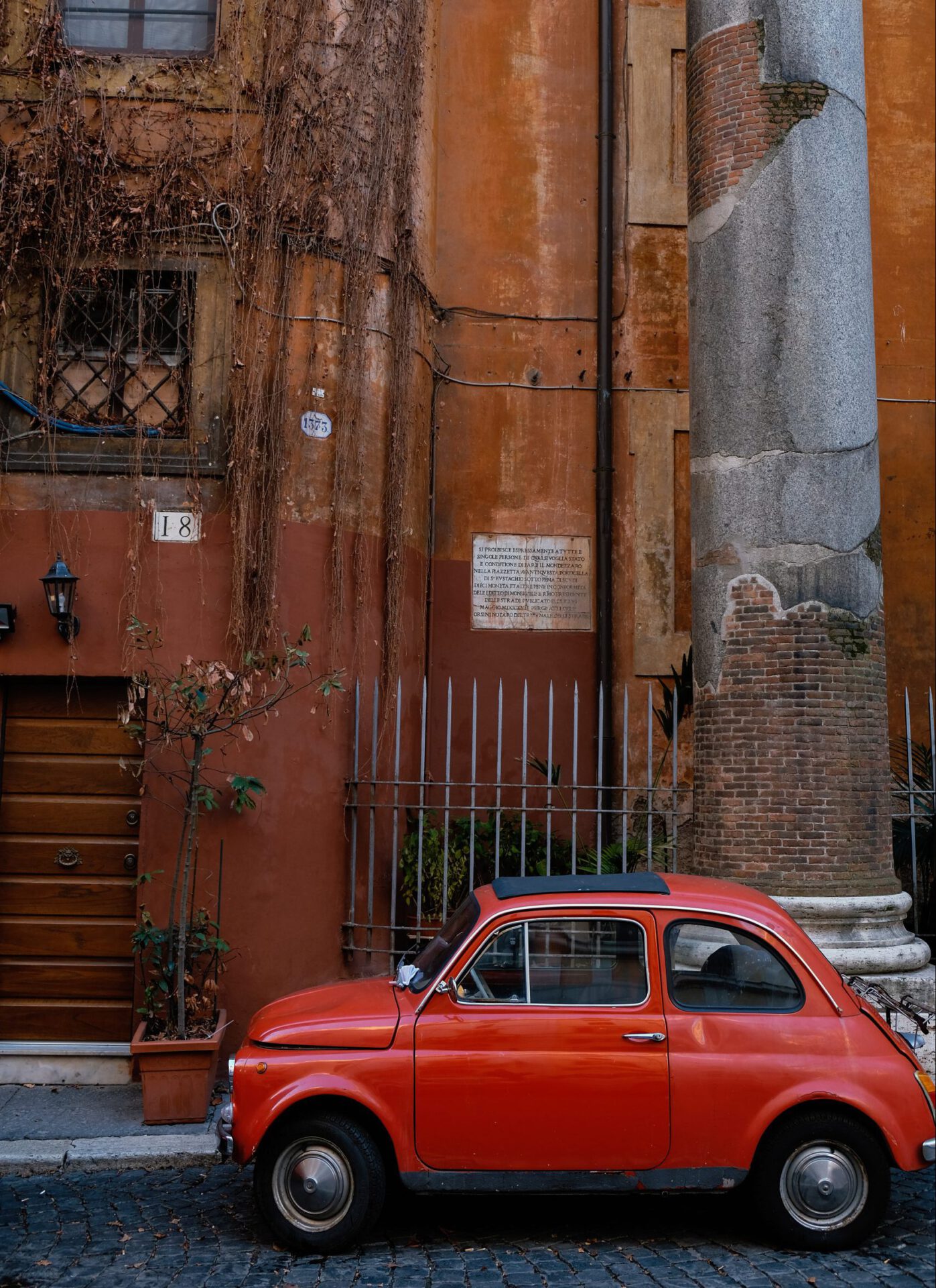 Red vintage fiat 500 on a street with red wall plants and column background in Italy