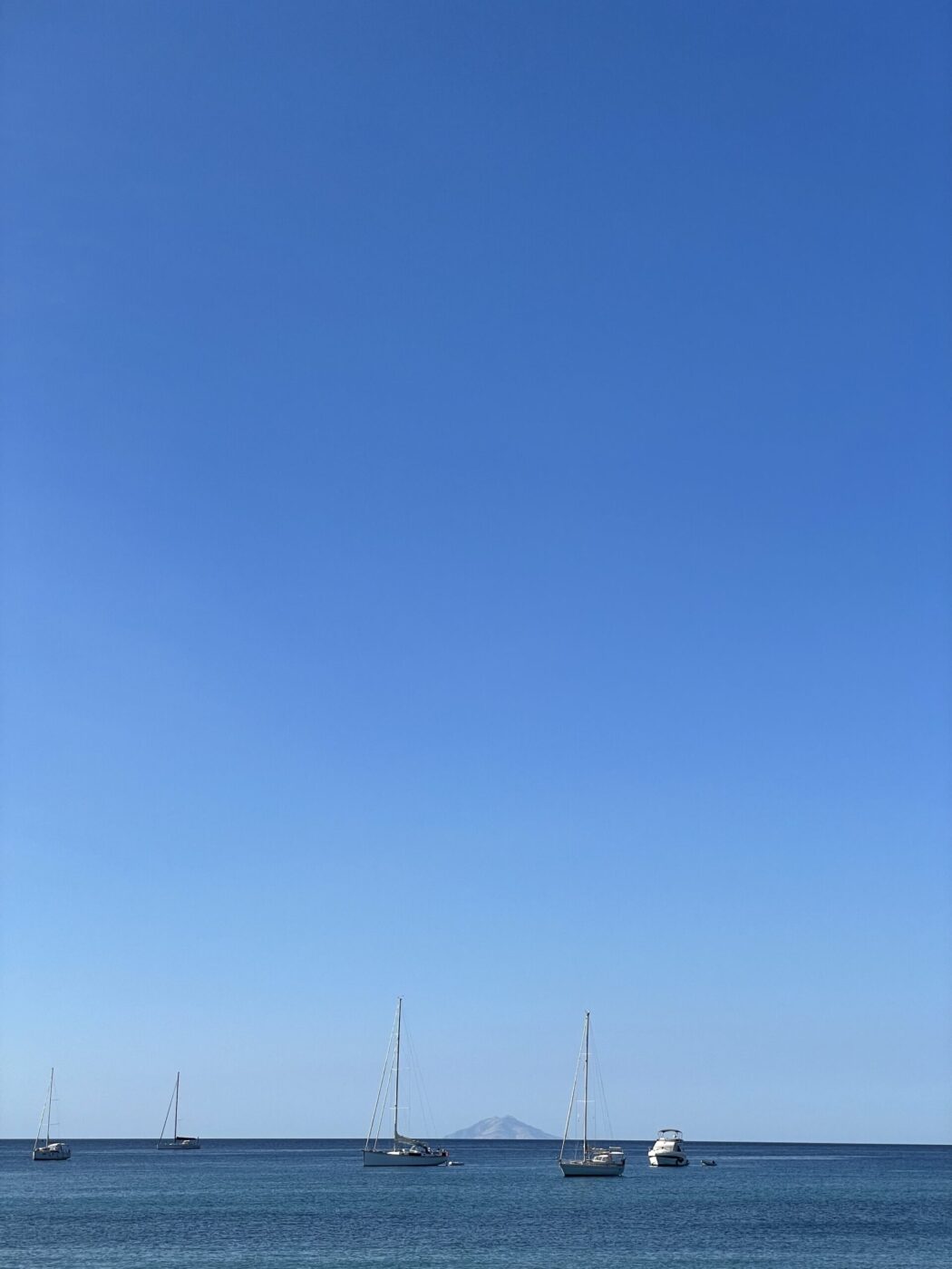 Boats and sailboats float on tranquil blue waters beneath a clear sky, a faint island visible on the far horizon.