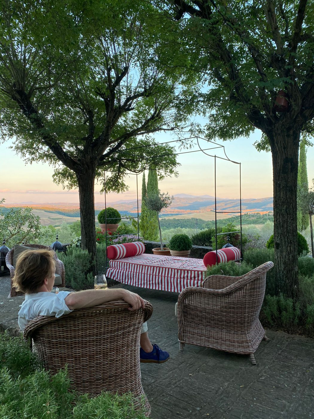 Woman drinking wine and seated on terrace with chairs and coach with green and sunset over mountains in the Arniano Painting School in Tuscany Italy