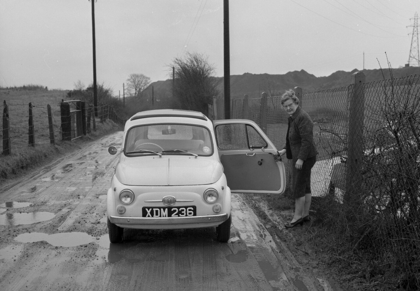 a black and white image of a woman standing outside a fiat