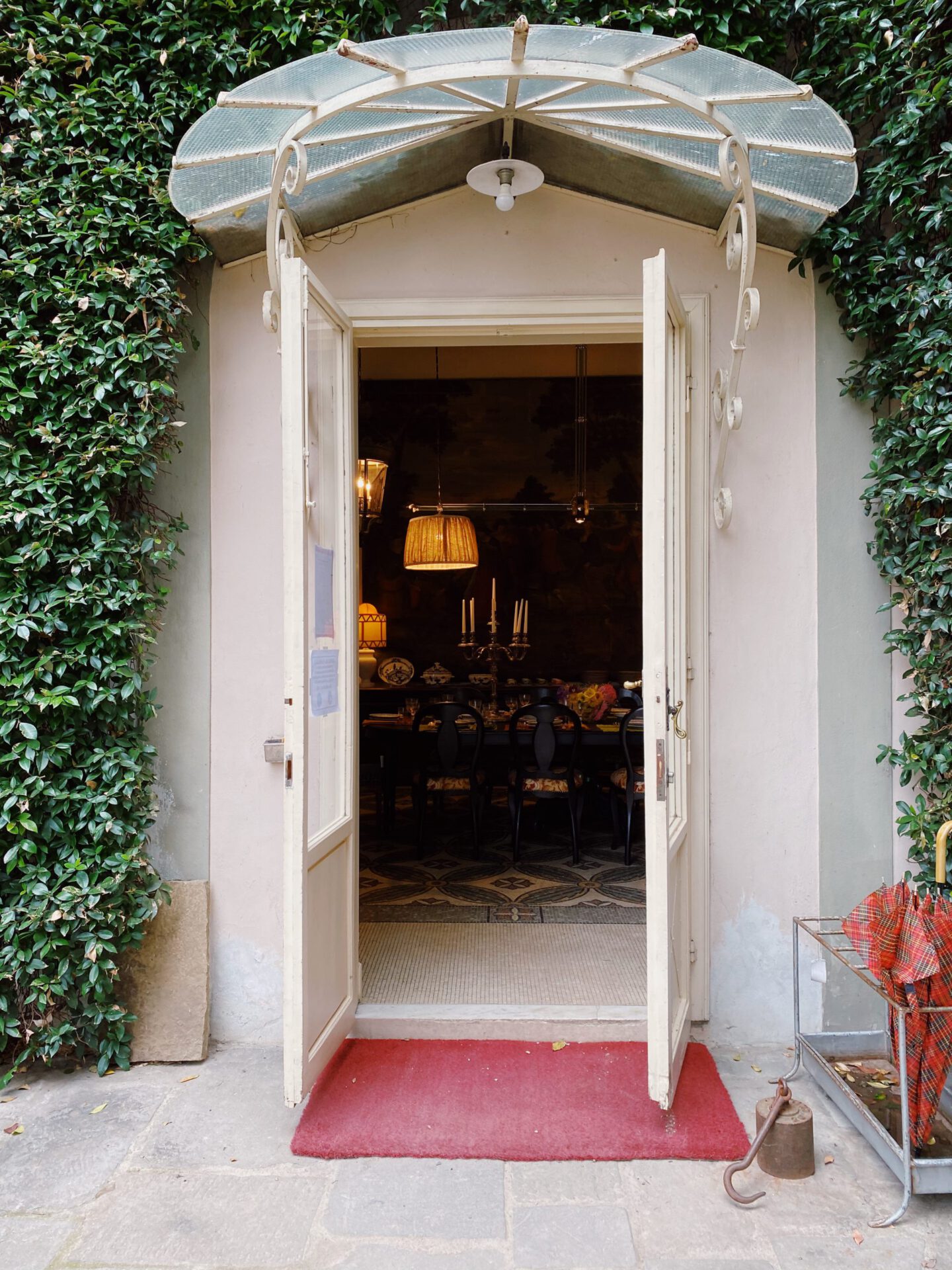 White door surrounded by plants wall and red carpet with a vintage dinning room filled with wooden furniture inside of Riccardo Barthel interior design showroom in Florence Tuscany in Italy