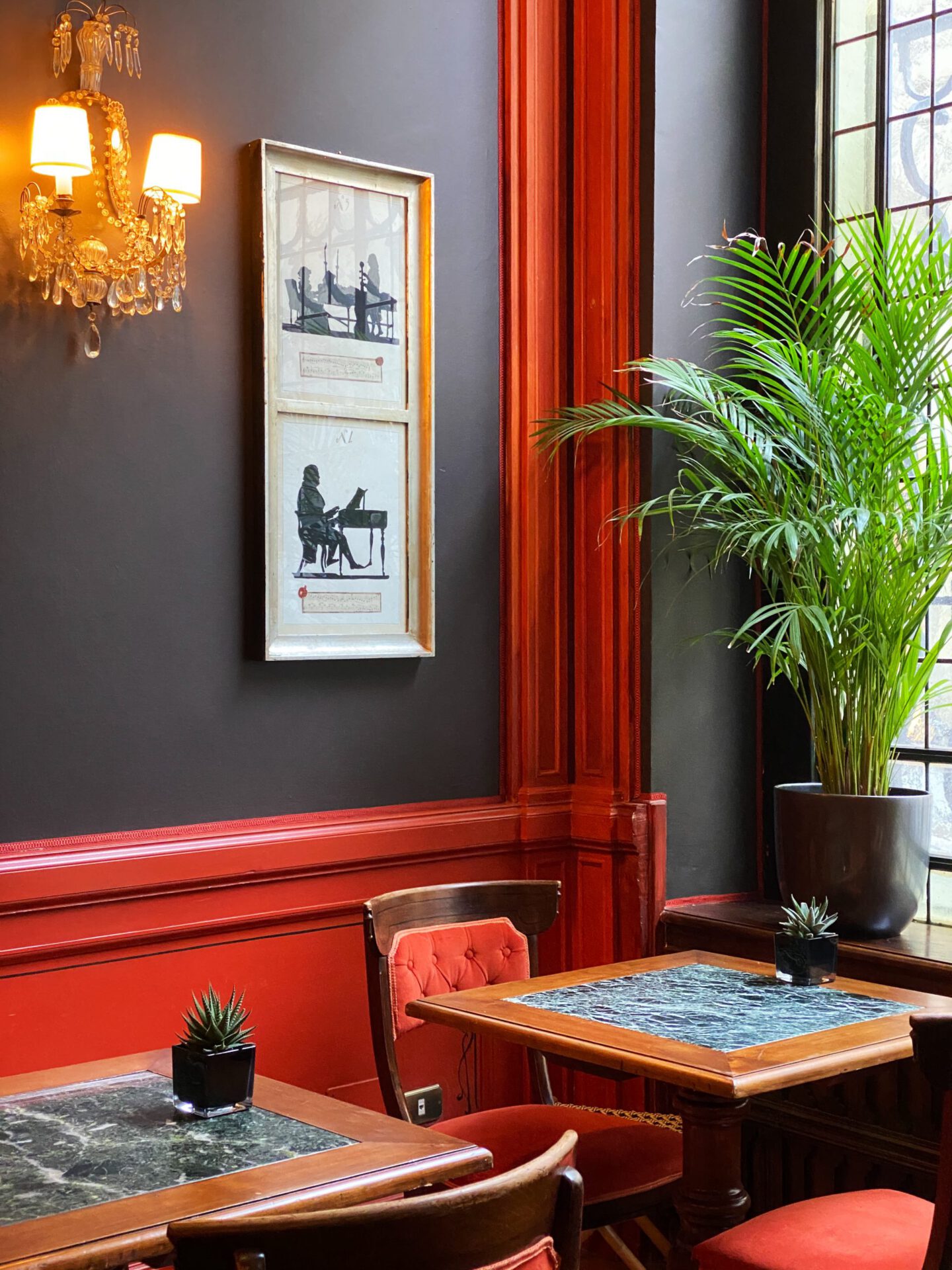 Fancy dinning room with dark and red walls wooden tables and red chairs with plants and luxury lamps at the Helvetia & Bristol hotel in Florence Tuscany in Italy