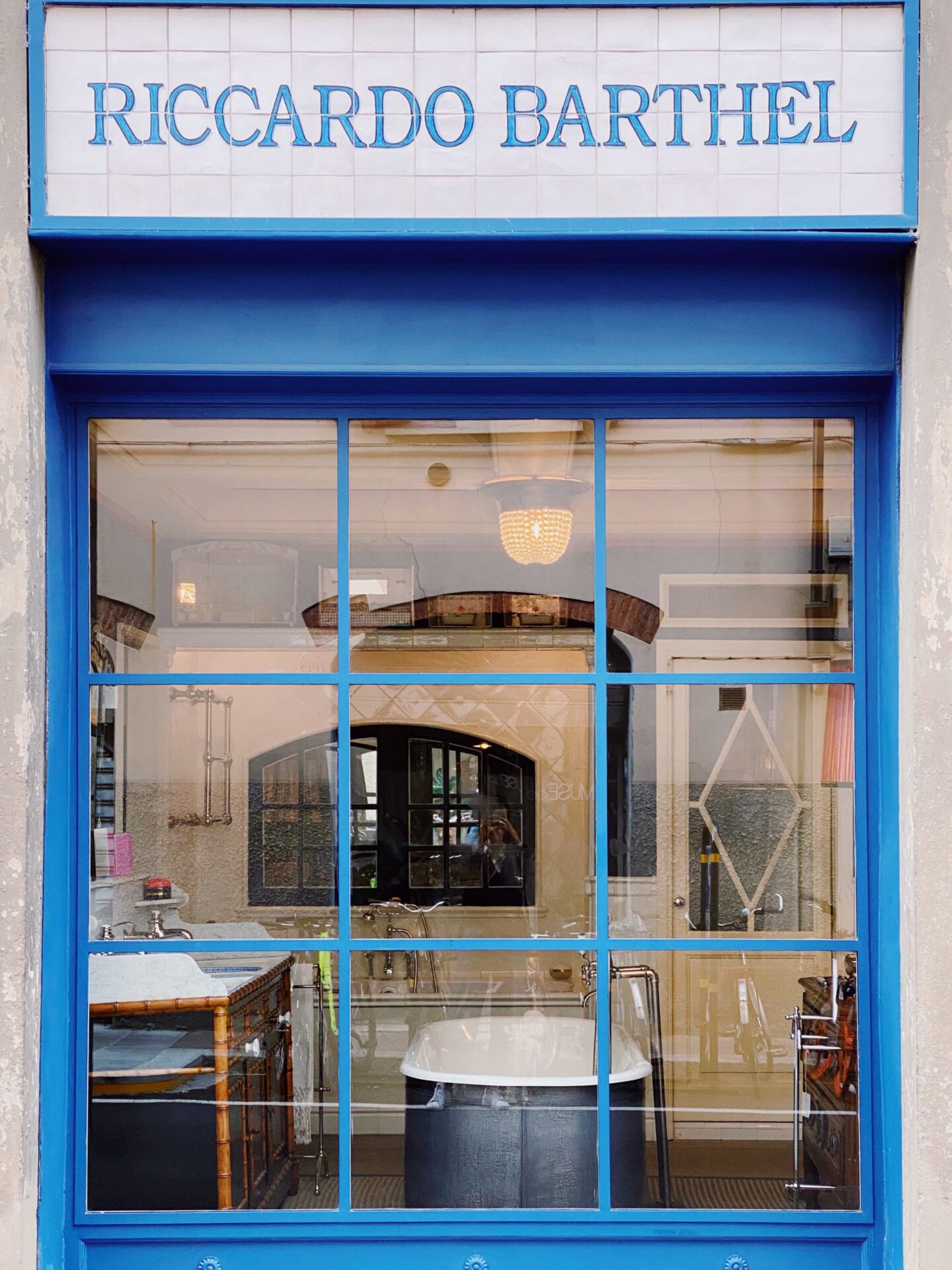 Blue window and shop sign in white ceramic with a vintage bathroom inside of Riccardo Barthel interior design showroom in Florence Tuscany in Italy