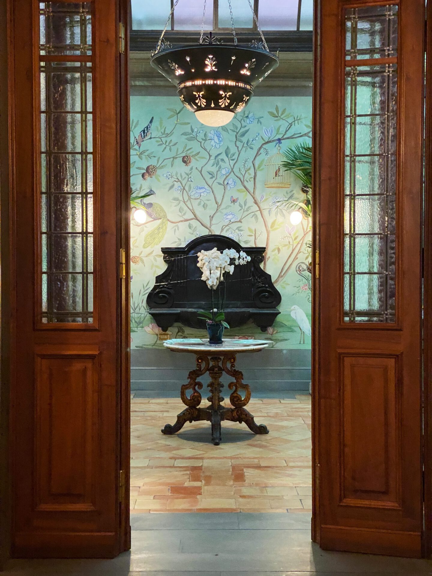 Marble and wooden table with flowers viewed from wooden and glass door with green flowers patterns wall at the Helvetia & Bristol hotel in Florence Tuscany in Italy