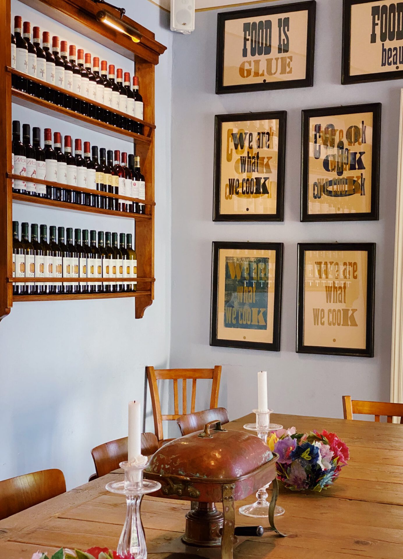 Vintage dinning room with wooden table stamped frames in the wall and wooden shelved filled with wine bottles inside of Riccardo Barthel interior design showroom in Florence Tuscany in Italy