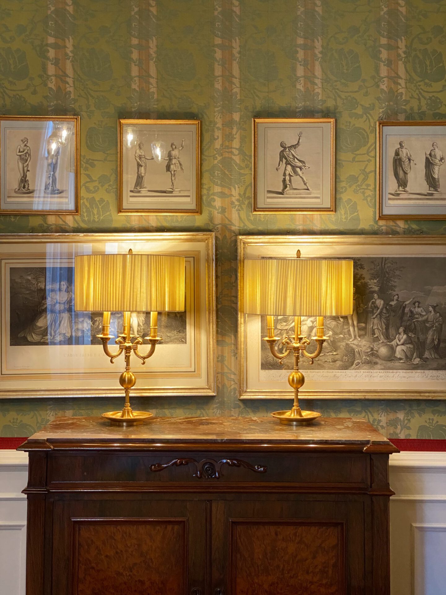 Luxury lamps over wooden shelf black and white frames over green patterned wall at the Helvetia & Bristol hotel in Florence Tuscany in Italy