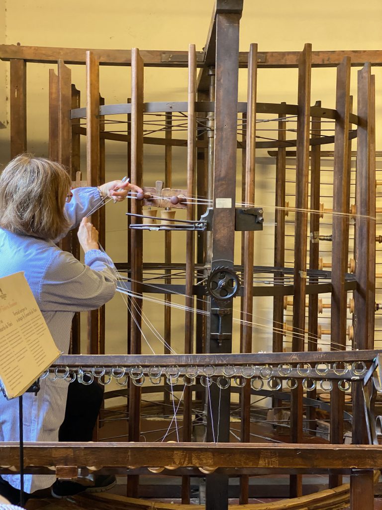 Woman working on a wooden antique silk warper with white threads in Old Silk Factory Setificio Fiorentino in Florence Tuscany in Italy