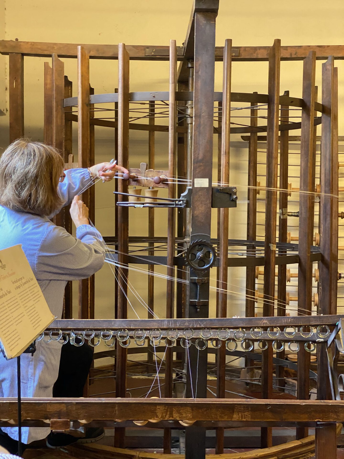 Woman working on a wooden antique silk warper with white threads in Old Silk Factory Setificio Fiorentino in Florence Tuscany in Italy