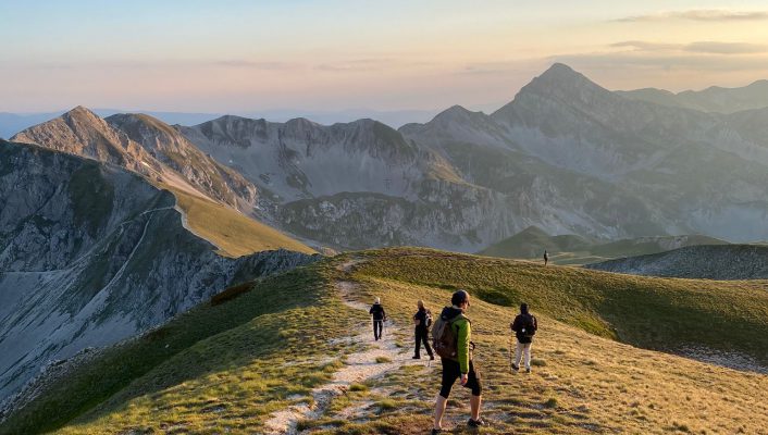 People hiking over huge chain of mountains with green and rocky floor at Gran sasso in Abruzzo Italy