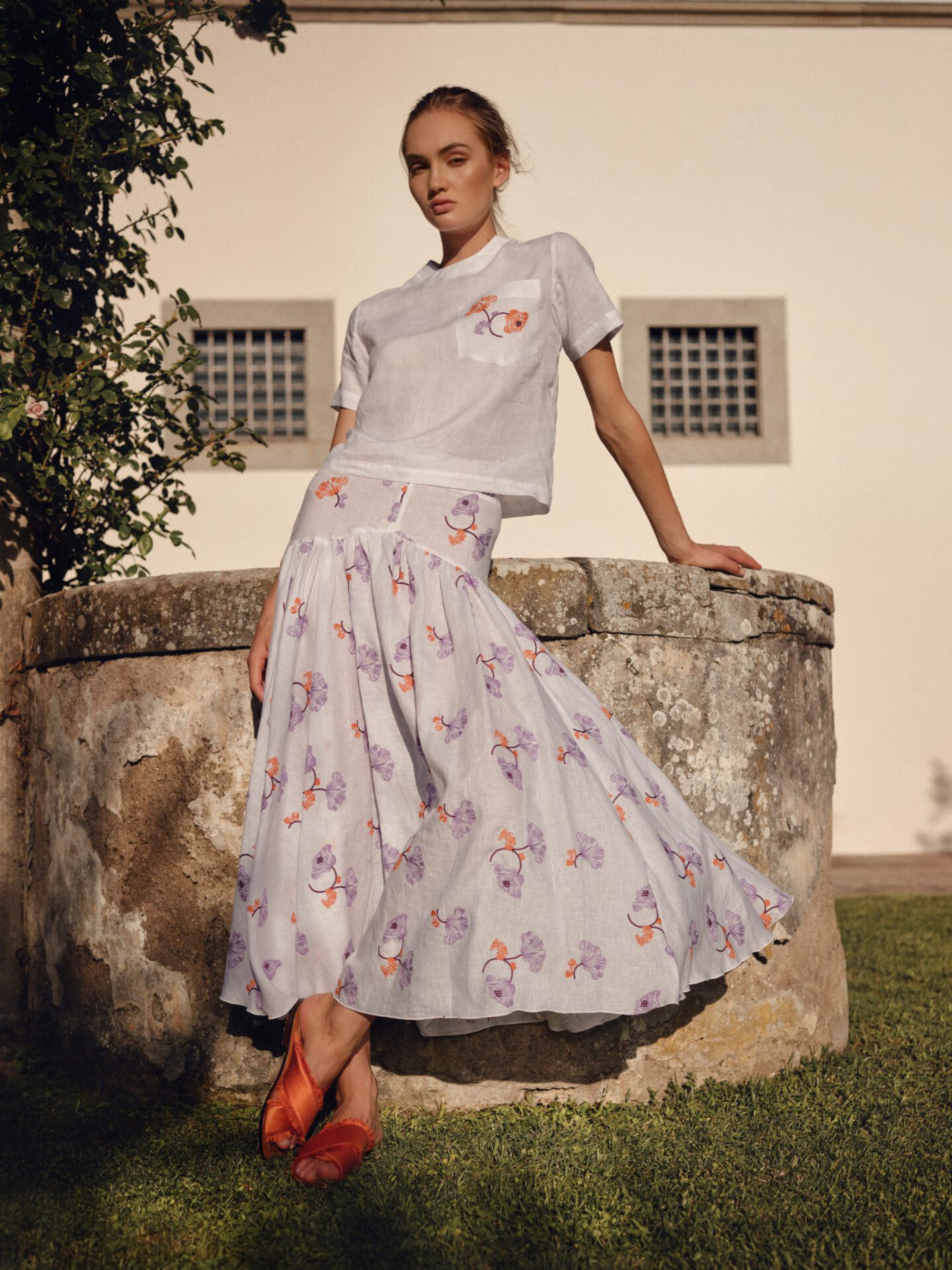 Woman possing with Caftanii white and patterned dress and sandals in grass and rustic surroundings in Italy