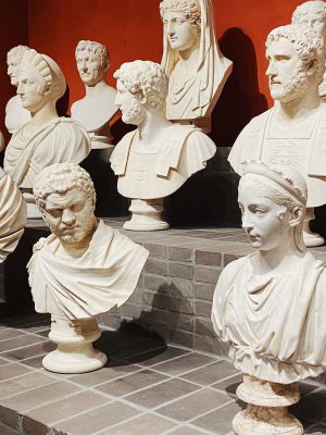 Marble busts of men and women from different ages over a bricked stair shelf with red background at Villa Caffarelli in Rome Lazio in Italy