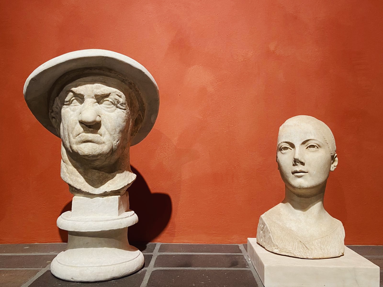 Marble busts of men and women over a bricked stair shelf with red background at Villa Caffarelli in Rome Lazio in Italy