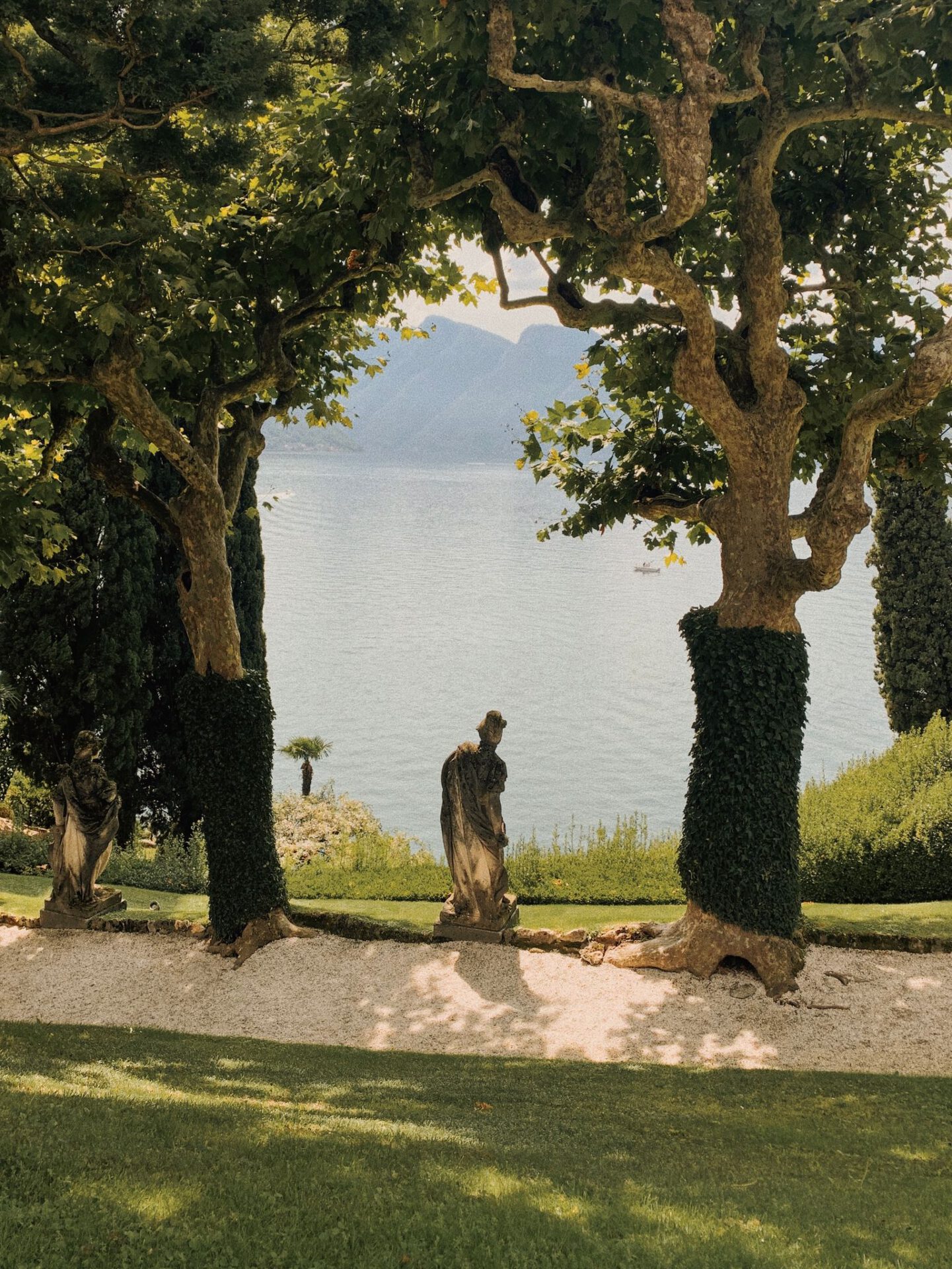 Antique sculpture surrounded by trees and plants viewing Lake Como and mountains in Lenno, Lombardy Italy