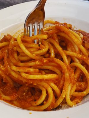 Italian Roman Roman Bucatini pasta All’Amatriciana over white plate and fork in restaurant