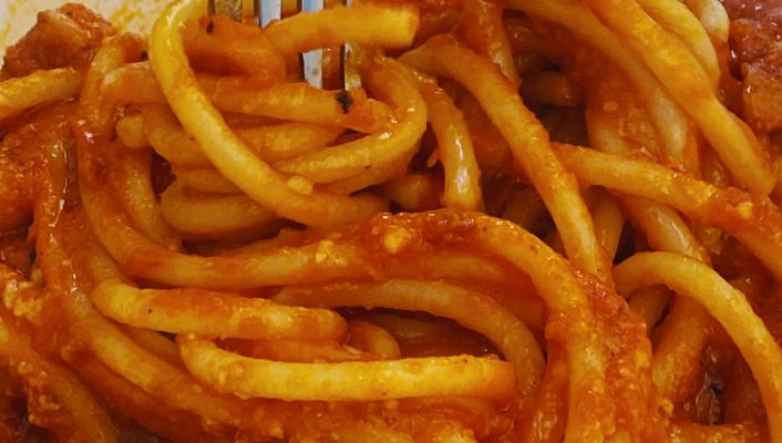 Italian Roman Roman Bucatini pasta All’Amatriciana over white plate and fork in restaurant