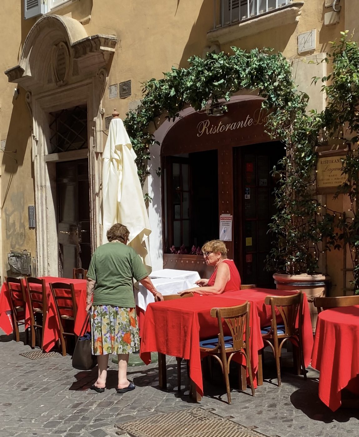 Lagana restaurant with outdoors red wooden tables and chairs in antique building with two old ladies talking in Rome Lazio in Italy