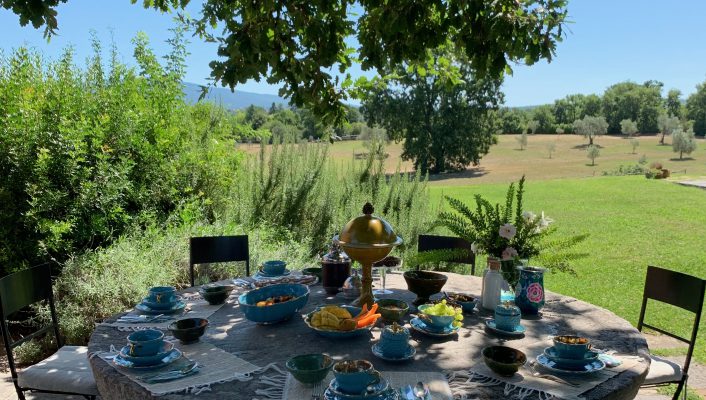 Circular rock table with metallic chairs filled with blue ceramic plates and cups for breakfast surrounded by plants and trees in an equestrian farm, Tenuta di Paternostro in Tuscia Italy