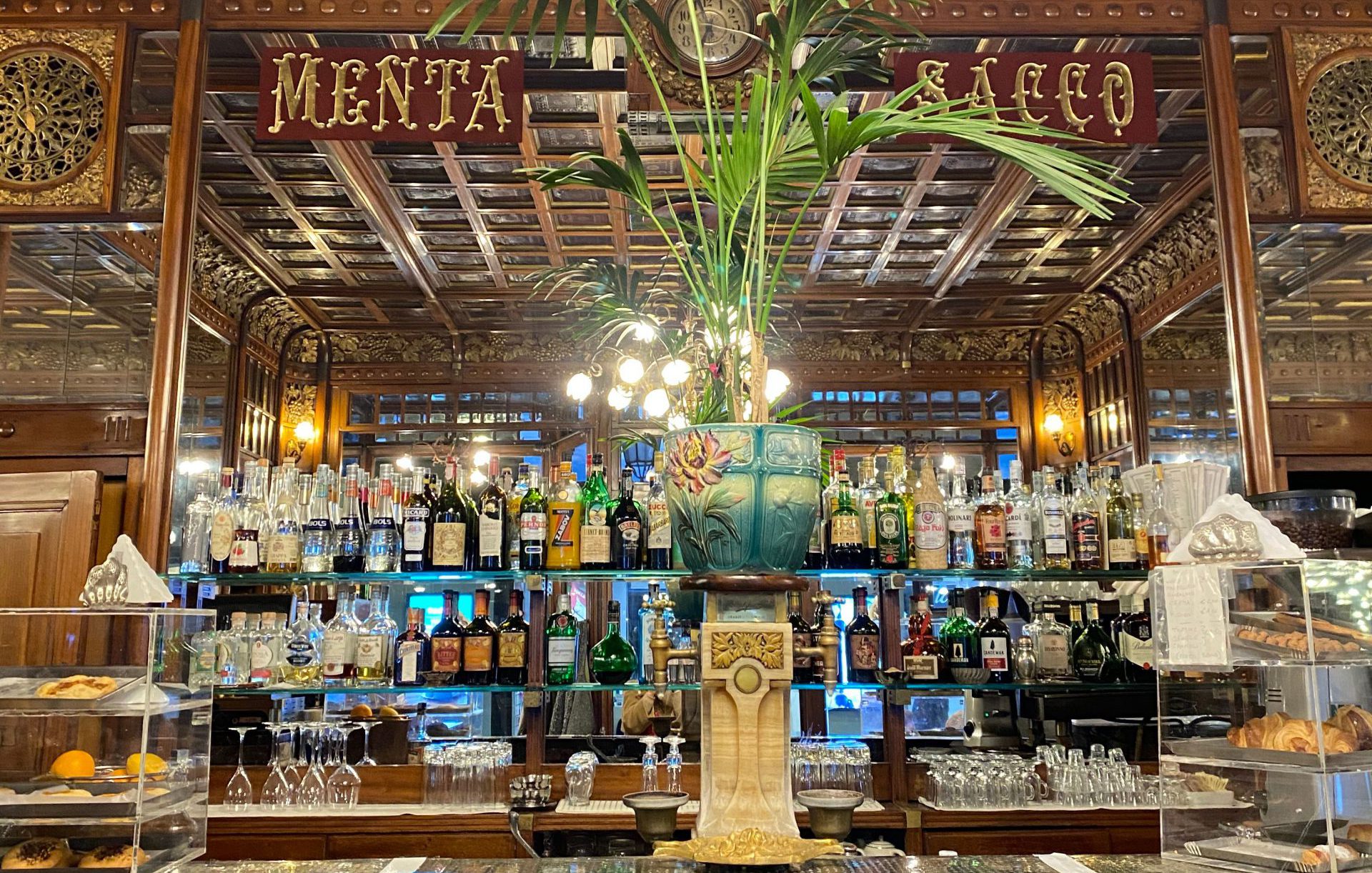 Antique bar counter with wooden structure and wall filled up with liquor bottles and plant on top at Caffè Mulassano in Turin Piedmont in Italy
