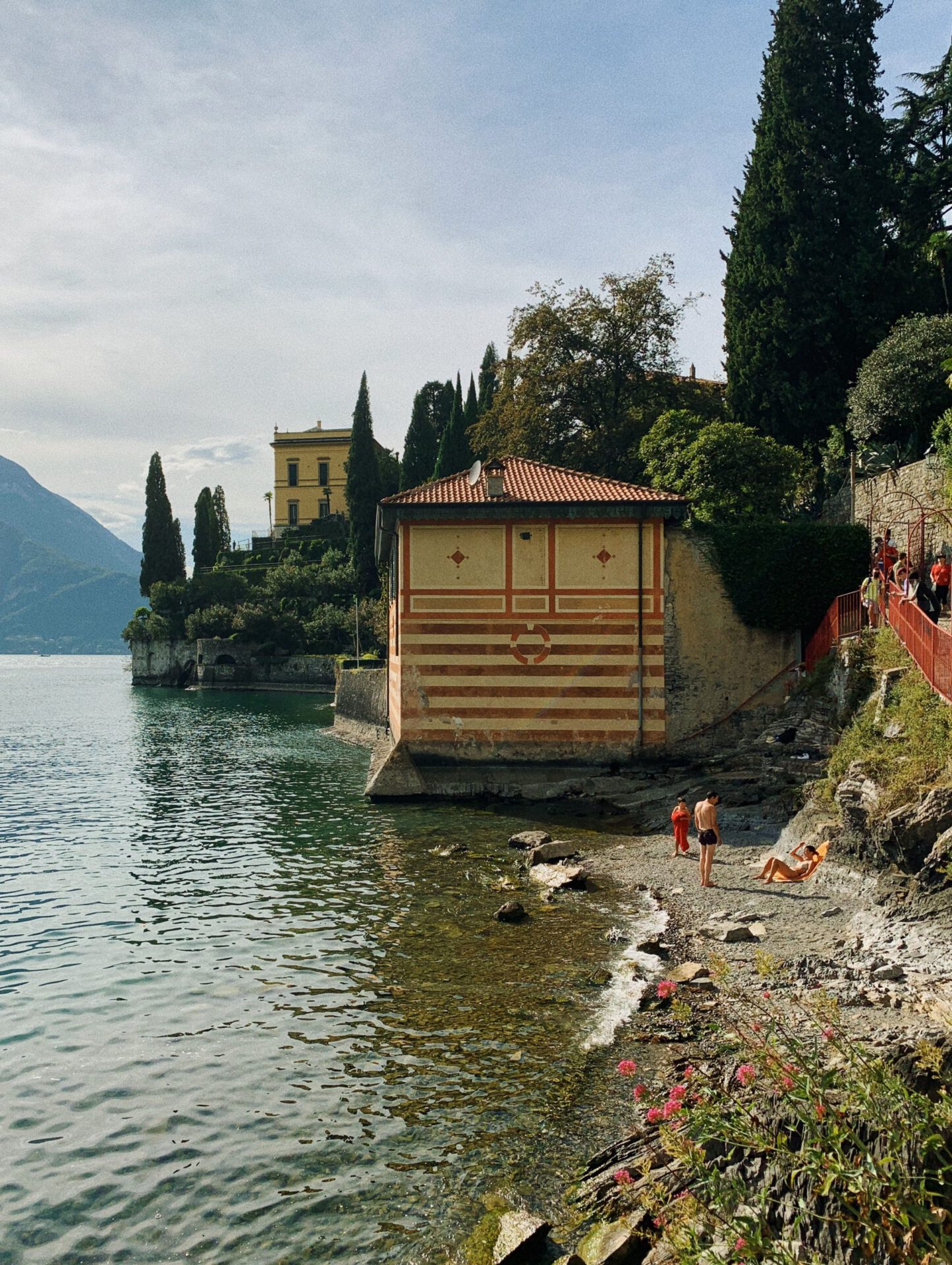 People swimming in Lake Como over the shore with mountains and antique houses in the background in Varenna Lombardy in Italy