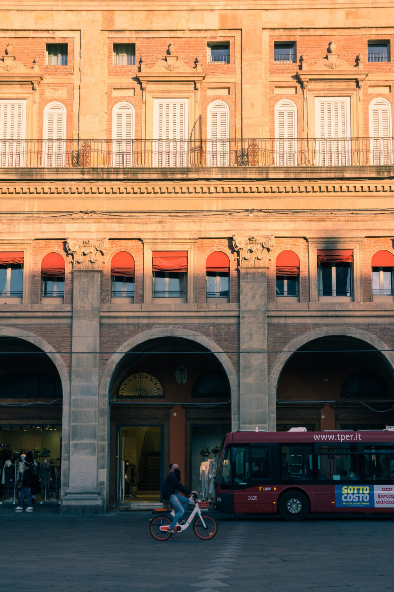 Old and historic building with antique style columns from the outside while a bus and bicycle cross in front in Bologna Emilia Romagna in Italy