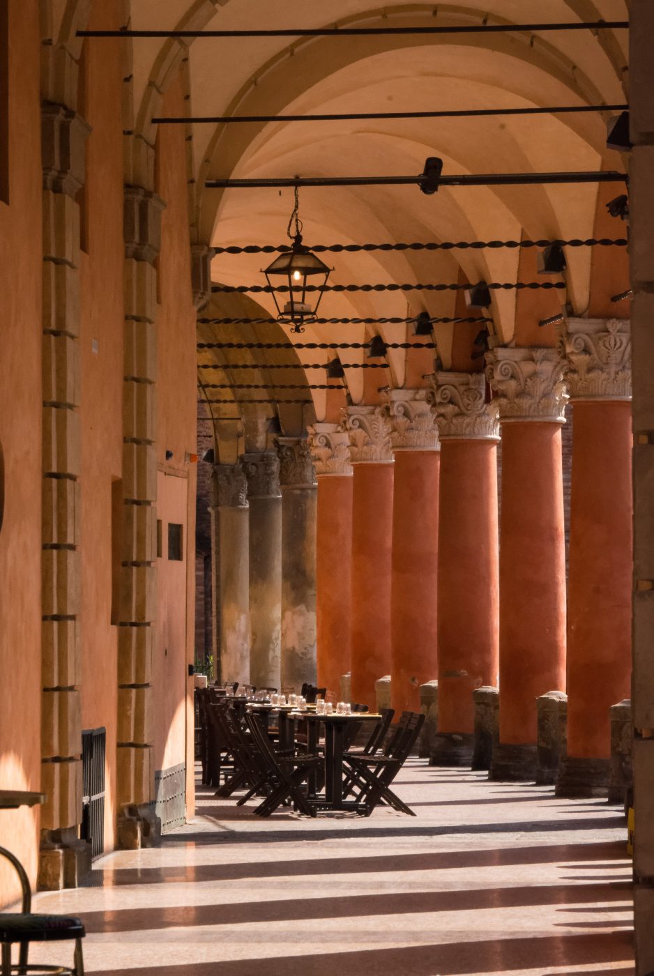 Tables and chairs under the porticoes with antique style columns and roof in Bologna Emilia Romagna in Italy