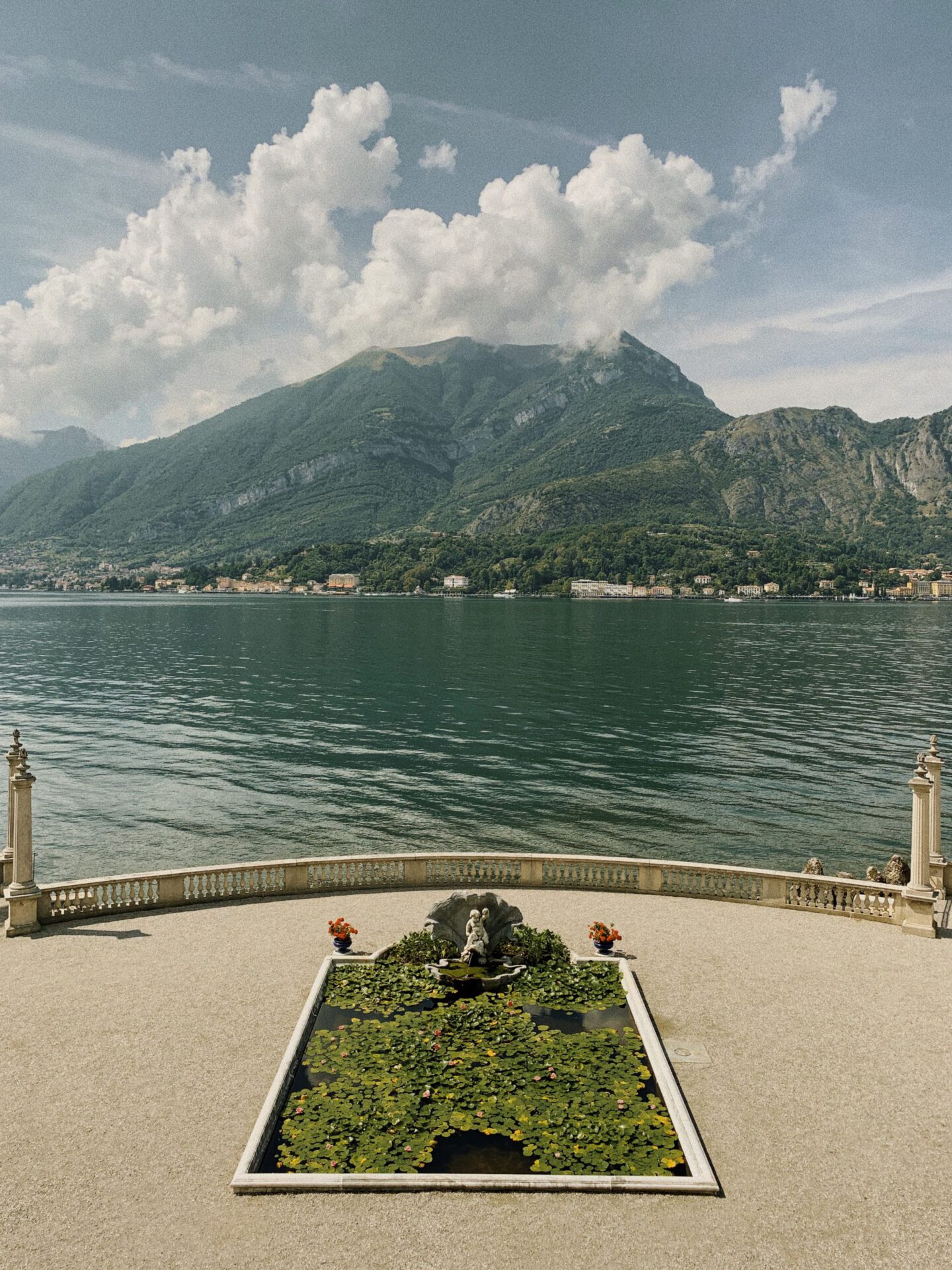 Antique sculptures over a terrace surrounded by plants and geometric fountian of Villa Melzi with lake como and mountains in the background in Bellagio Lombardy in Italy