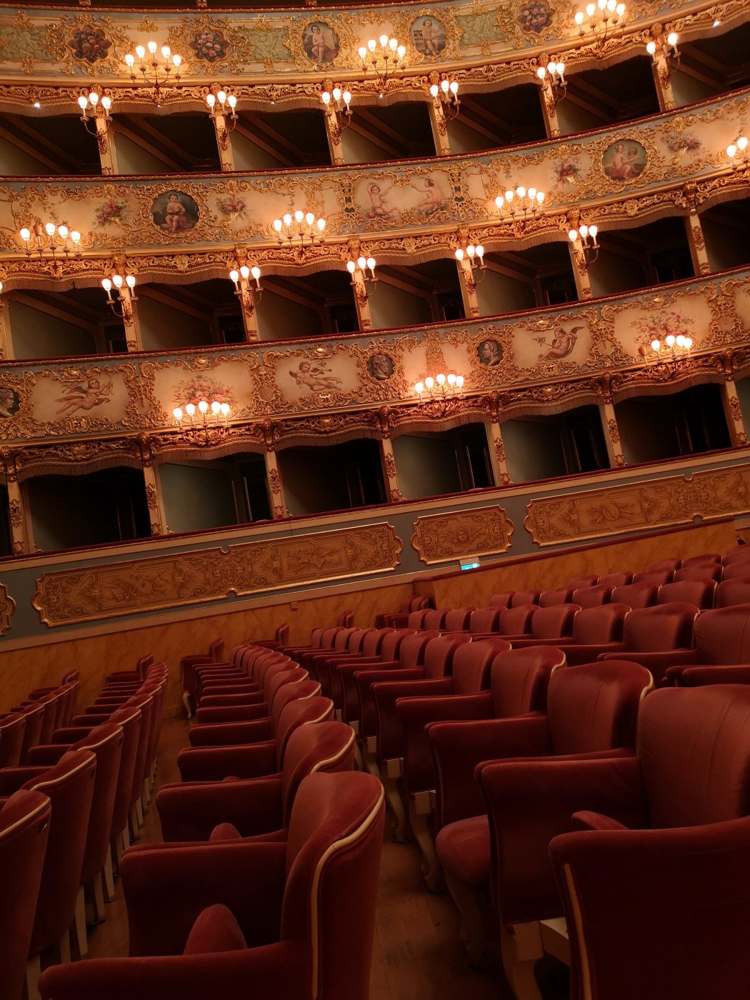Theater red chairs in rows with balconies antique paintings candle lamps and low illumination at The Phoenix in Venice Veneto in Italy