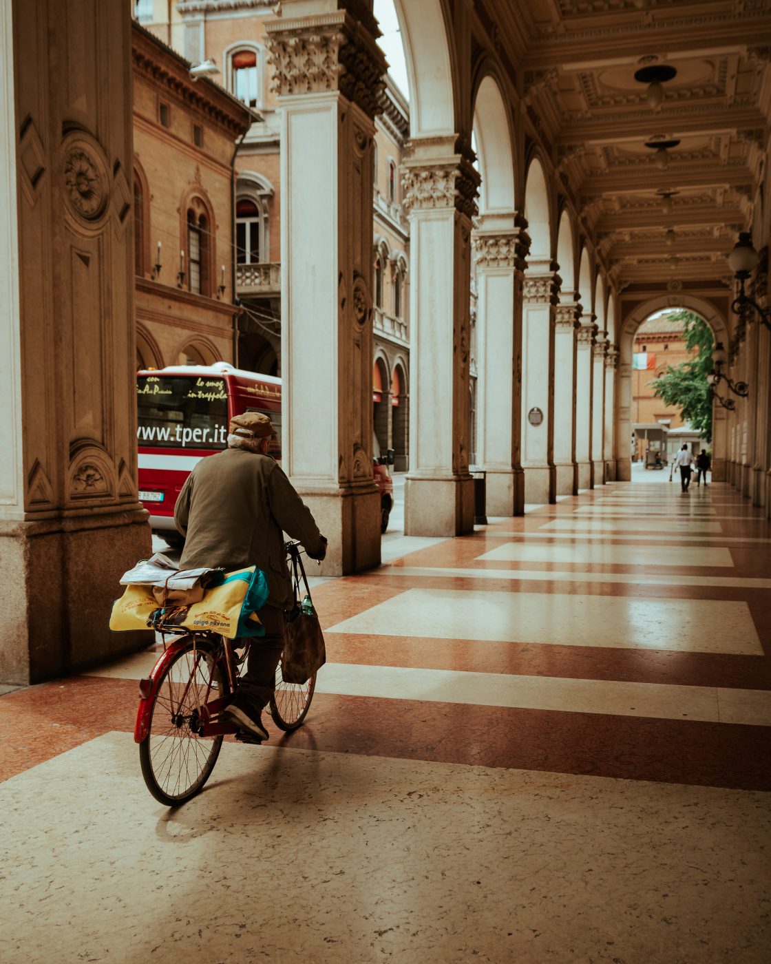 Man riding a bicycle under the porticoes with antique style columns and roof in Bologna Emilia Romagna in Italy