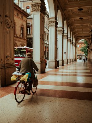 Man riding a bicycle under the porticoes with antique style columns and roof in Bologna Emilia Romagna in Italy