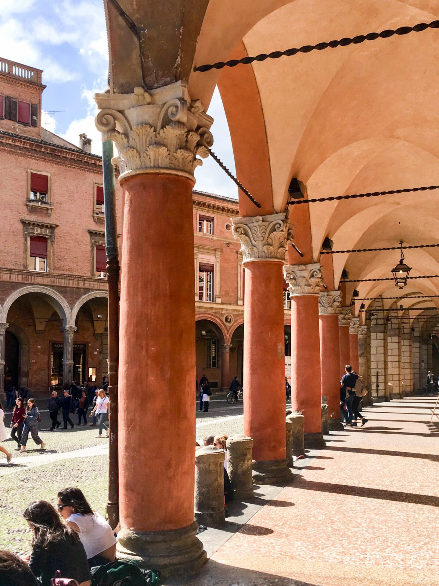 People seated and walking under the porticoes with antique style columns and roof in Bologna Emilia Romagna in Italy