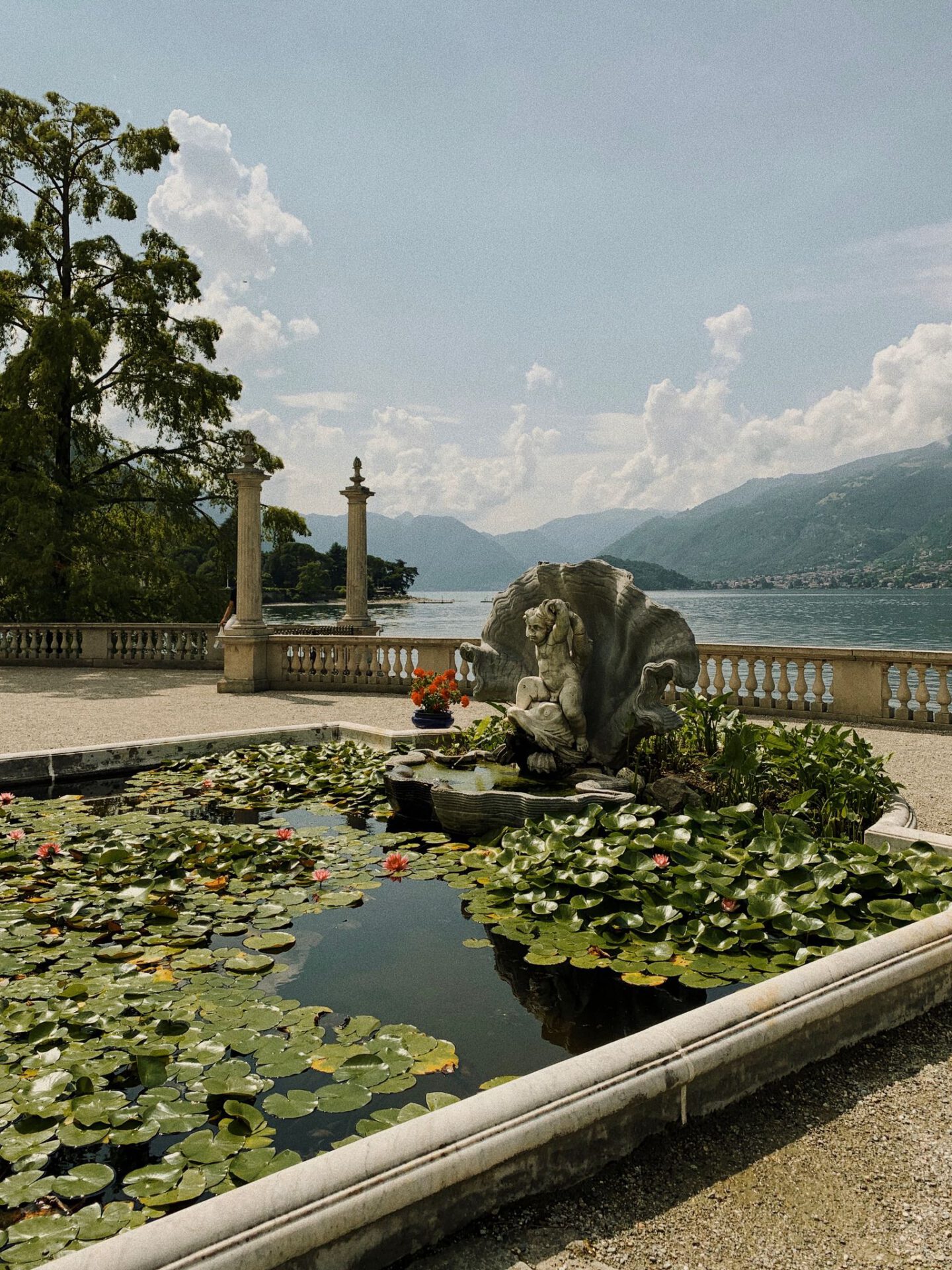 Antique sculptures over a terrace surrounded by plants and geometric fountian of Villa Melzi with lake como and mountains in the background in Bellagio Lombardy in Italy