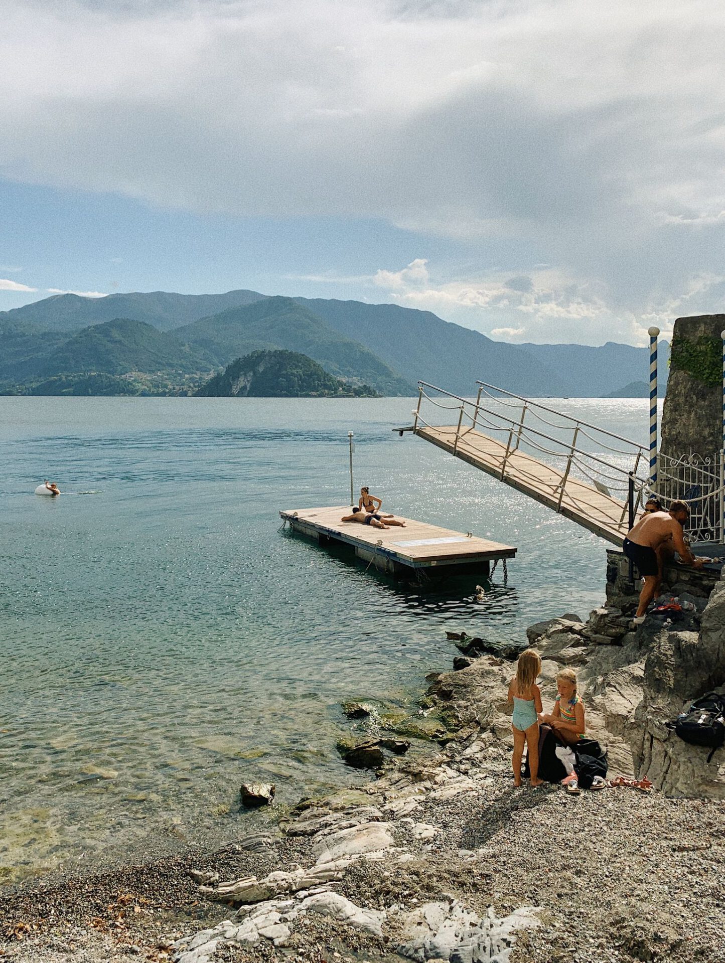 People swimming in Lake Como over the shore with mountains in the background in Varenna Lombardy in Italy