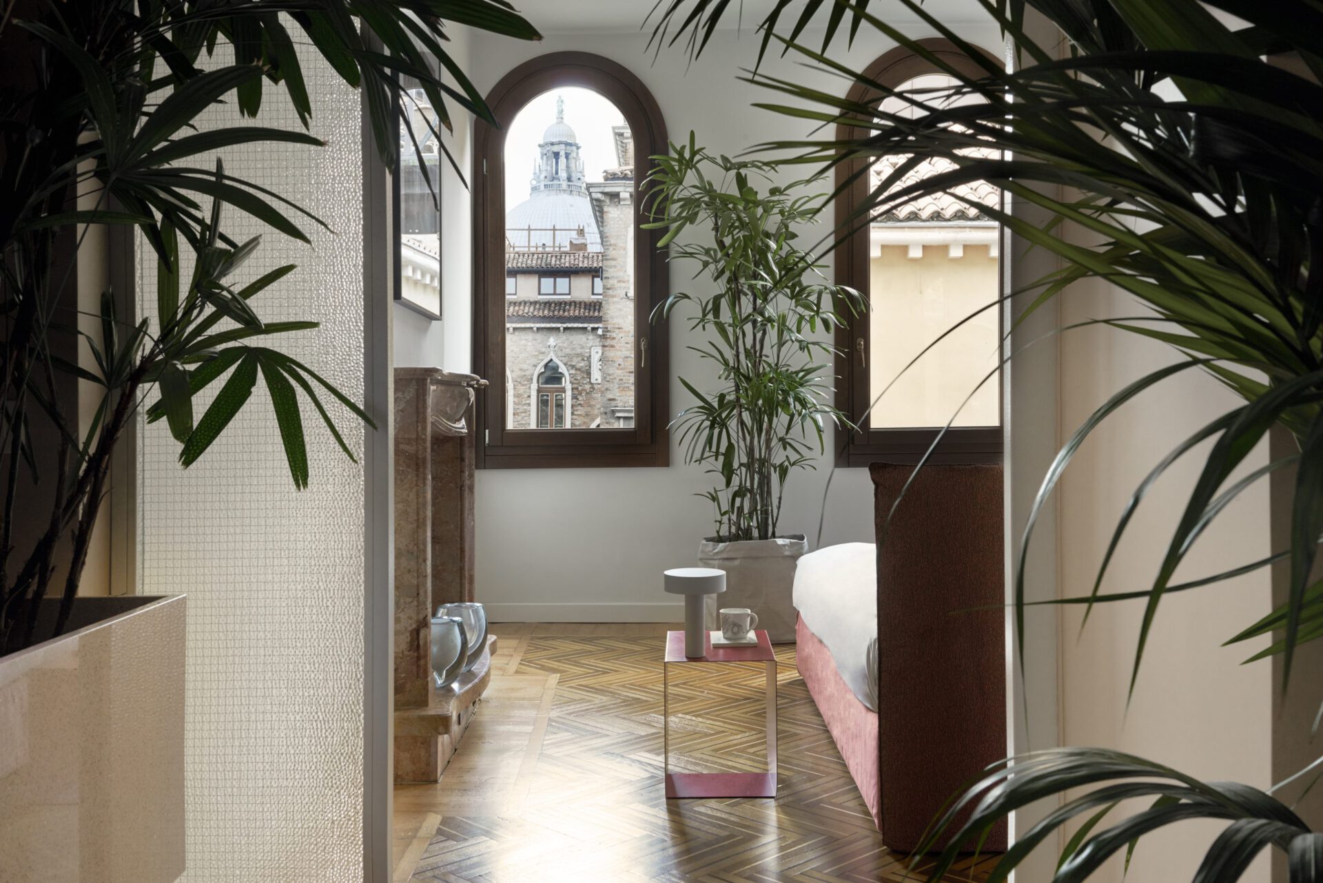 Minimalistic style bedroom surrounded by plants, modern walls and arched windows viewing to antique buildings in Hotel Flora in Venice Veneto in Italy