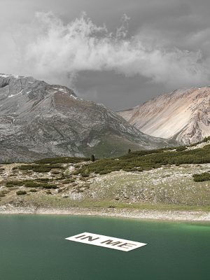 IN ME sign floating in a blue lake in the mountains surrounded by mountains and snow at SMACH art park in Val Badia in Alto Adige Italy