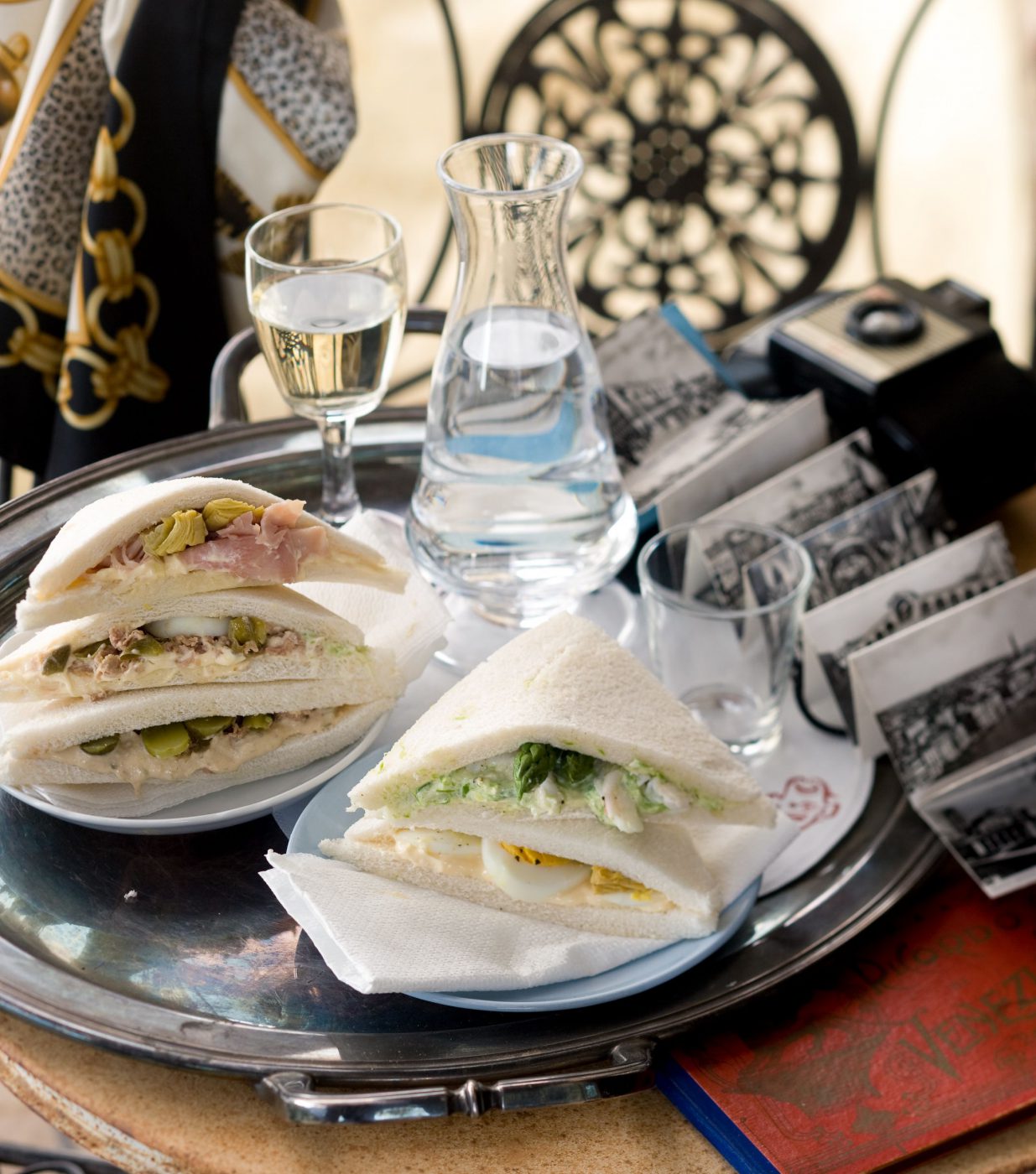 Typical tramezzini sandwiches next to water cups in a silver colored tray in a typical bar in venice