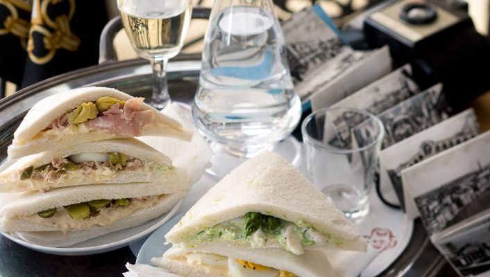 Typical tramezzini sandwiches next to water cups in a silver colored tray in a typical bar in venice