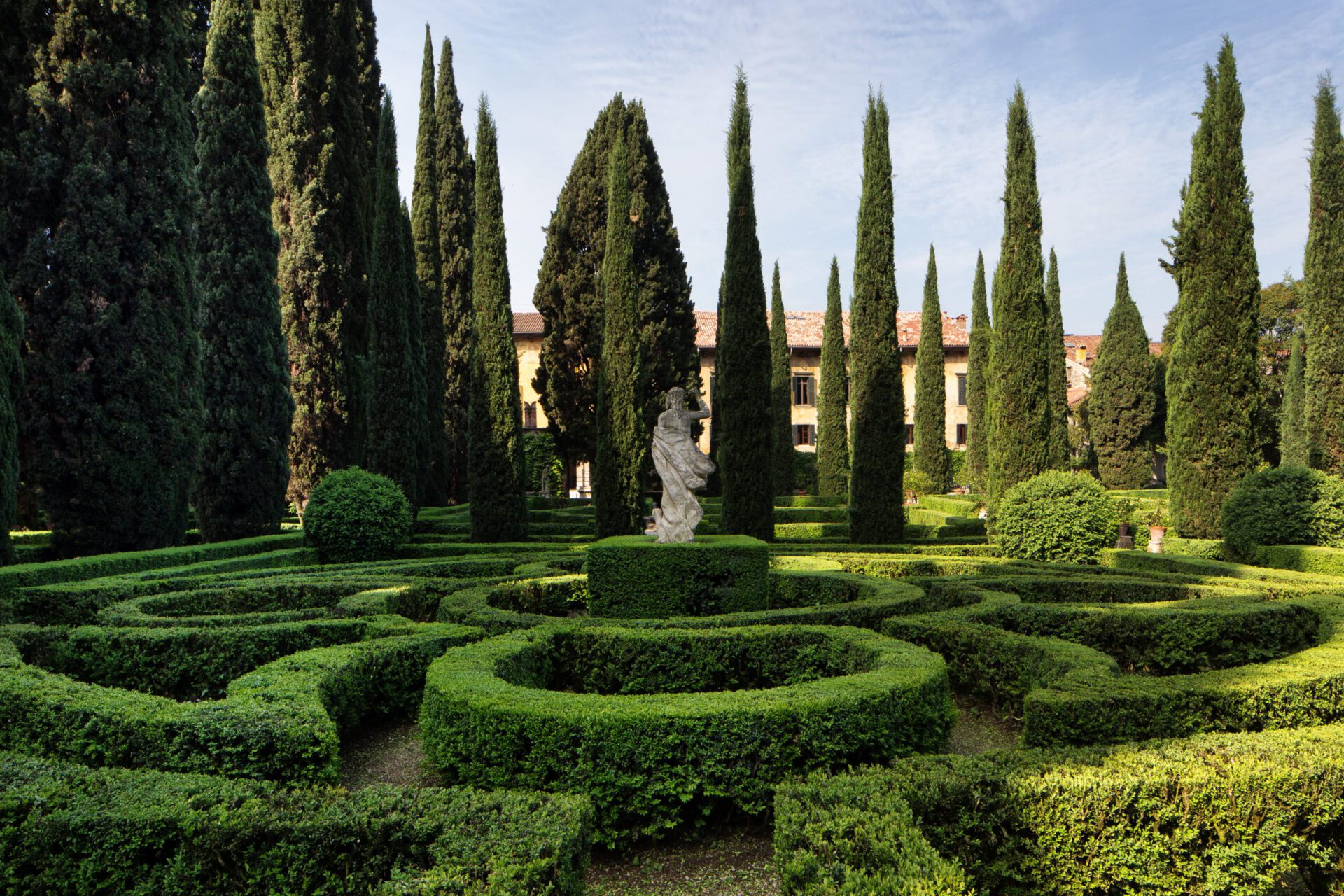 Geometric shaped garden with bushes and tall trees behind a antique building at the Giardino Giusti in Veneto Italy