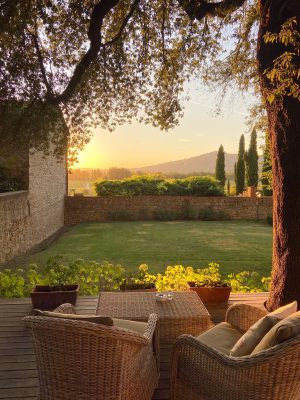 Wooden chairs and table over wooden terrace viewing green landscape and rocks house with sunset background at Villa di Piazzano in Cortona Tuscany in Italy