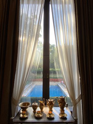 Blue outdoors swimming pool viewed from a window with white curtains and golden jars at Villa Necchi Campiglio in Milan Lombardy in Italy